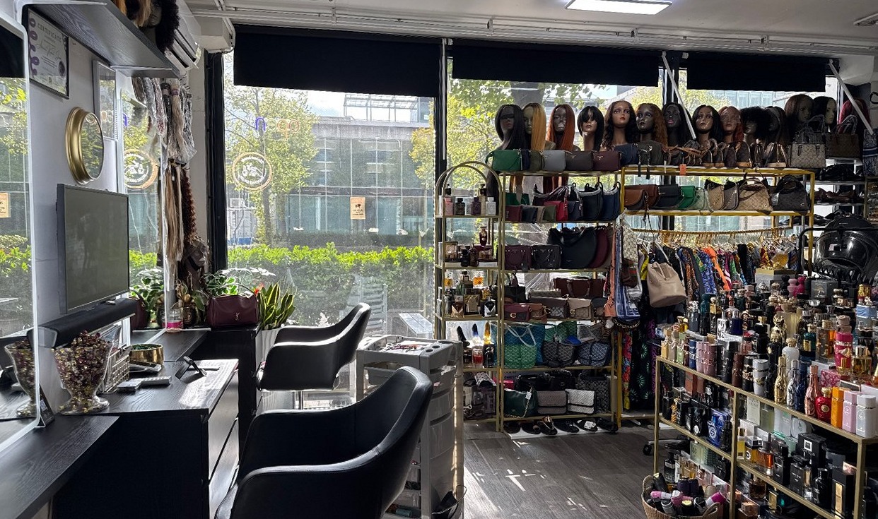 De salon aan de Volmerlaan: zwarte salonstoelen bij het raam, gouden rekken met tassen en een rij pruiken langs de wand